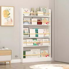 a white book shelf filled with books in a living room next to a dresser and chair