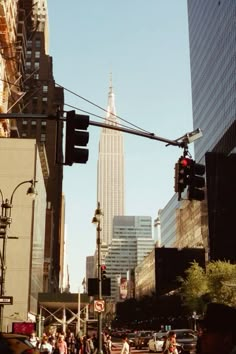 people are crossing the street in front of tall buildings and skyscrapers on a sunny day