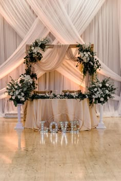 a table topped with flowers and candles on top of a hard wood floor covered in white drapes