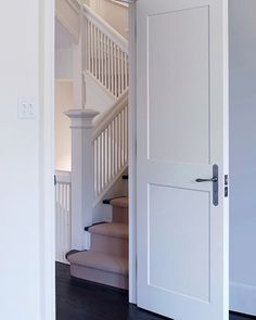 an open door leading to a stairway in a white house with wood floors and handrails