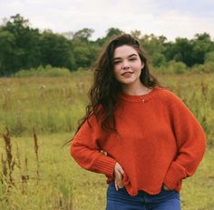 a woman in an orange sweater is posing for the camera with her hands on her hips