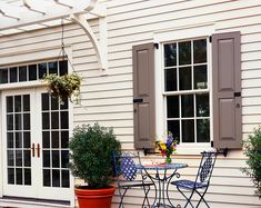 an outdoor table and chairs with potted plants in front of a white house on a sunny day