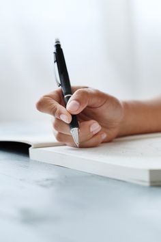 a woman's hand holding a pen and writing on a notebook