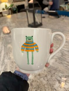 a person holding up a coffee cup with a bear on it's sleeve and an orange striped sweater