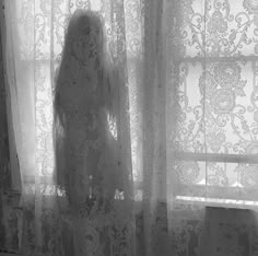 the shadow of a woman standing in front of a window next to a sheer curtain