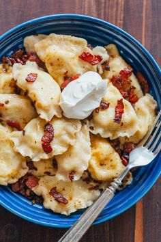 a blue bowl filled with pasta covered in cheese and bacon next to a silver fork