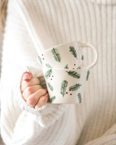 a woman holding two cups in her hands with christmas decorations on them and pine cones