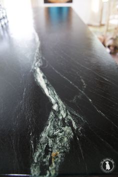 a black marble counter top with white and green streaks on the surface in front of a dining room table