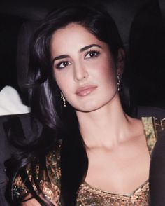 a woman sitting in the back seat of a car with long black hair and earrings on