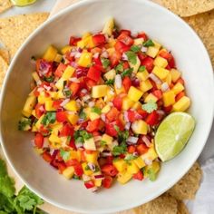 a white bowl filled with mango salsa and tortilla chips next to lime wedges