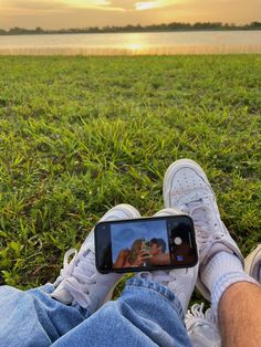 a person taking a selfie with their cell phone in front of the lake at sunset