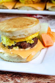 a breakfast sandwich with eggs, sausage and cheese on a white plate next to carrots