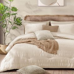 a bed with white comforter and pillows in a room next to a potted plant