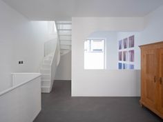 an empty room with white walls and stairs leading up to the second floor, next to a wooden cabinet