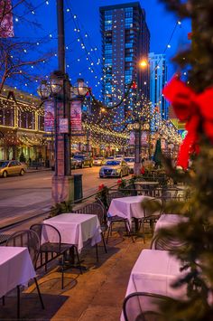 tables and chairs are set up on the sidewalk in front of buildings with christmas lights