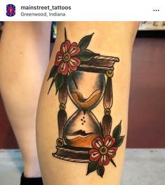 a tattoo on the leg of a woman with an hourglass and flowers in it