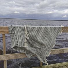 a blanket draped over a wooden rail by the water's edge on a cloudy day