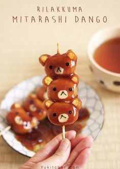 there is a hand holding some food on a stick with teddy bears on it and a cup of tea in the background