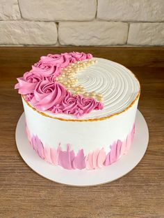 a white cake with pink frosting and flowers on top is sitting on a wooden table