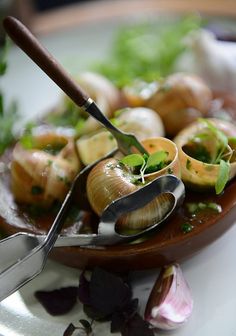 a plate full of snails and greens with a pair of tongs