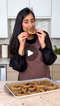 a woman in an apron is eating food from a pan on the kitchen counter top