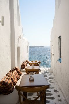 an alley way with tables and chairs next to the ocean on a sunny day in mykonos, greece