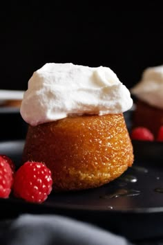 two desserts with whipped cream and raspberries on a black plate next to each other