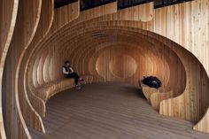 a person sitting on a bench in a room with wooden walls and flooring that looks like a spiral staircase