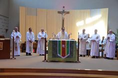 a group of men standing in front of a cross on top of a church pew