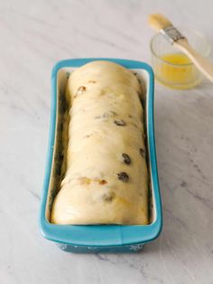 a loaf of bread in a blue dish next to a glass container with orange juice