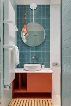 a bathroom with blue tiles and orange accents on the counter, along with a round mirror