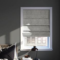 a living room with a window covered in roman shades and a lamp on the end table