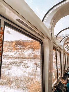 the interior of a train with snow on the ground and mountains in the distance as seen from inside