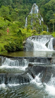 a man standing on top of a waterfall next to a lush green forest