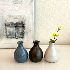 three vases with yellow flowers in them sitting on a table next to a painting