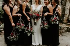 a group of women standing next to each other in front of a stone building holding bouquets