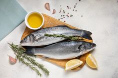 two fish sitting on top of a wooden cutting board next to lemons and spices