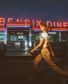 a woman walking down the street in front of a diner with neon signs on it