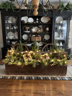 a dining room table decorated for christmas with greenery and lights in the centerpiece