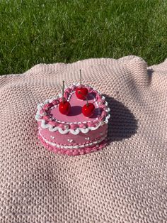 a pink cake with two cherries on it sitting on a blanket in the grass