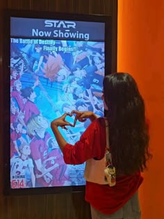 a woman making a heart shape with her hands while standing in front of a poster