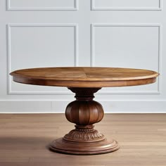 a round wooden table on a hard wood floor with white walls in the back ground