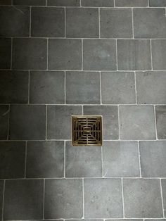 a floor grate in the middle of a tile floor with a drain on it