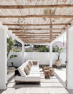 an outdoor covered patio with white couches and wooden beams on the ceiling, surrounded by potted plants