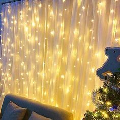 a living room decorated for christmas with lights on the curtains and a teddy bear decoration