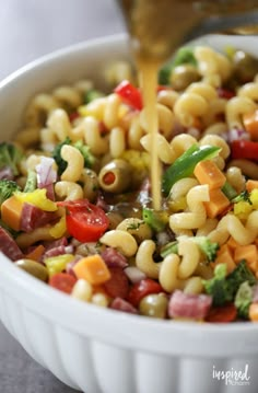 a bowl filled with pasta and vegetables being drizzled on top of it