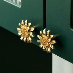 pair of gold sunflower earrings on green cabinet