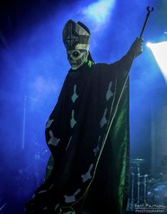 a man dressed up as a skeleton holding a stick in his right hand while standing on stage