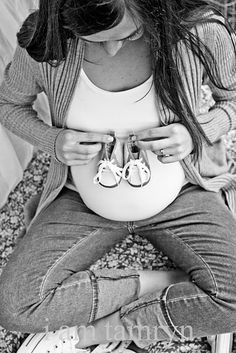 a pregnant woman sitting on top of a bed with her shoes hanging off the belly