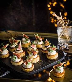 small appetizers are arranged on a black tray with lights in the back ground